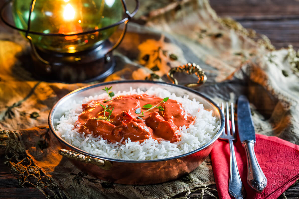 Braces-Friendly Diet - A delectable plate of creamy curry served over a bed of fluffy white rice, perfectly suited for a braces-friendly diet. The meal, garnished with fresh herbs, offers a soft texture that is gentle on braces, minimizing the risk of discomfort. The dish is presented in a decorative metal bowl, placed on a rustic table setting with a warm, ambient glow from a nearby lantern. A knife and fork rest on a folded red napkin beside the bowl, suggesting a cozy dining experience. The scene emphasizes enjoying flavorful, soft foods that are easy to chew while wearing braces.