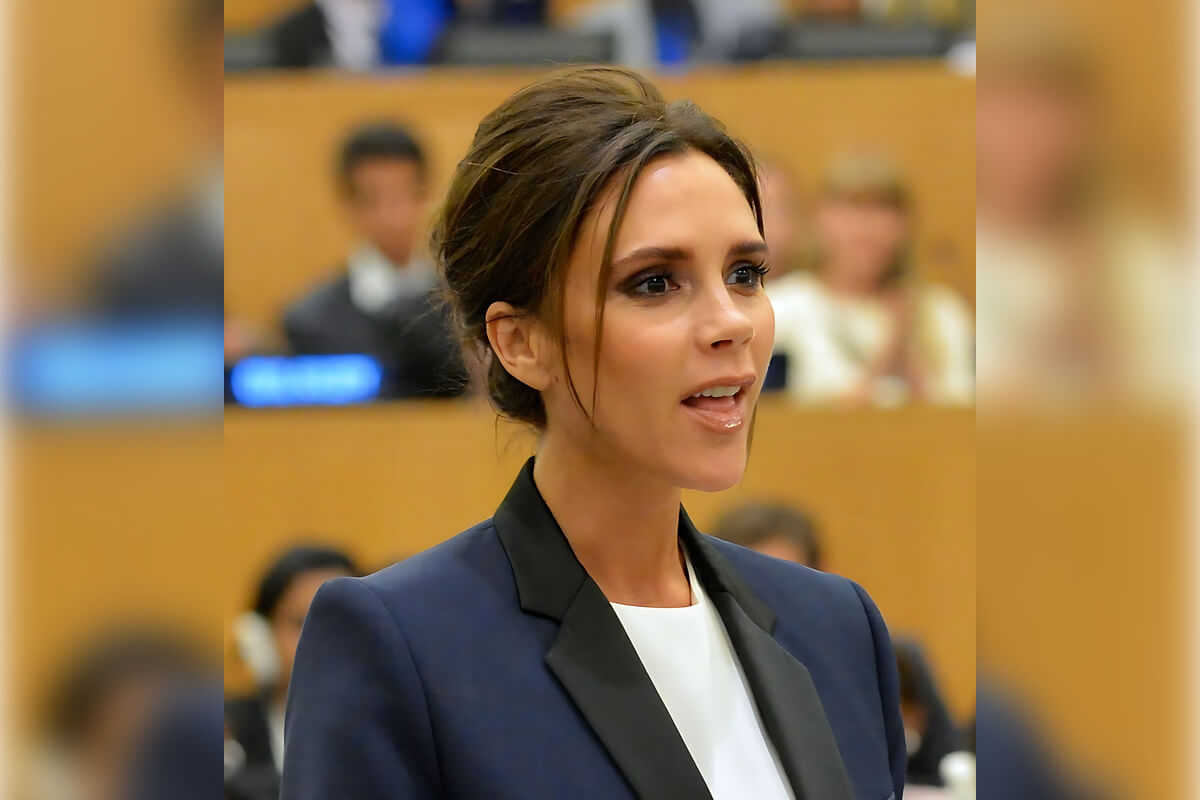 5 Celebrity Smiles - A female celebrity is speaking at a formal event, exuding a confident and engaging presence. She is dressed in a tailored, dark blazer over a light blouse, embodying a professional and polished look. Her hair is styled in a chic updo, with a few strands framing her face. The setting appears to be a conference or a public speaking engagement, indicated by the audience members visible in the blurred background and the formal atmosphere. Her expression is focused yet relaxed, showcasing her commitment to the subject at hand while maintaining her signature poise and style.